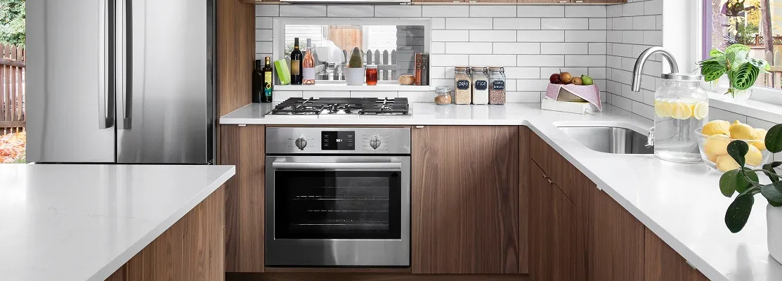 Modern kitchen with wood cabinetry, stainless steel appliances, white countertops, and subway tile backsplash